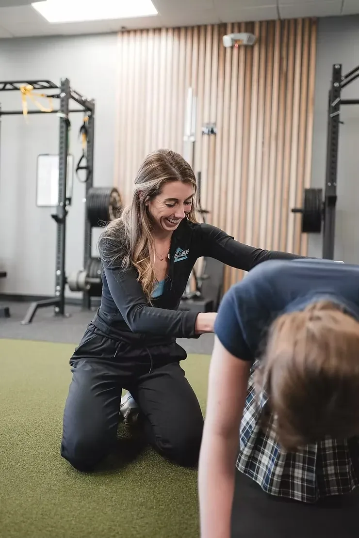 A clinician kneeling on the turf guiding a patient through a standing assessment at Streamline Performance Physical Therapy in Phoenix, AZ