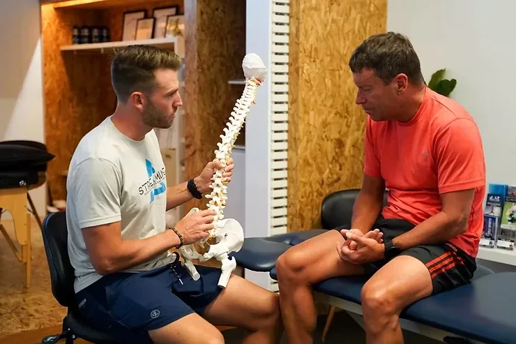 A clinician holding an articulated spine model while explaining a plan to a patient at Streamline Performance Physical Therapy in Phoenix, AZ