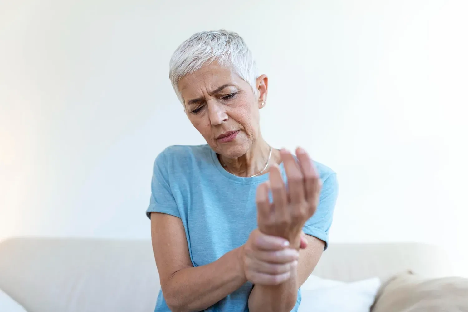An older woman wincing as she flexes and holds her hand and wrist