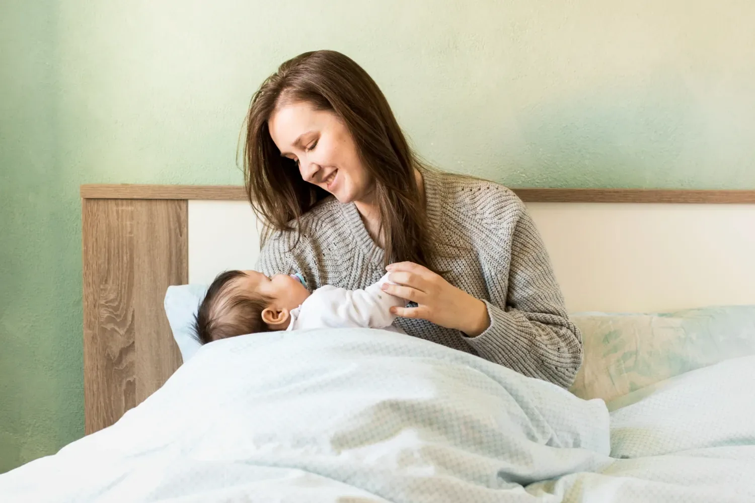 A woman sitting up in bed smiling down at a swaddled newborn in her arms