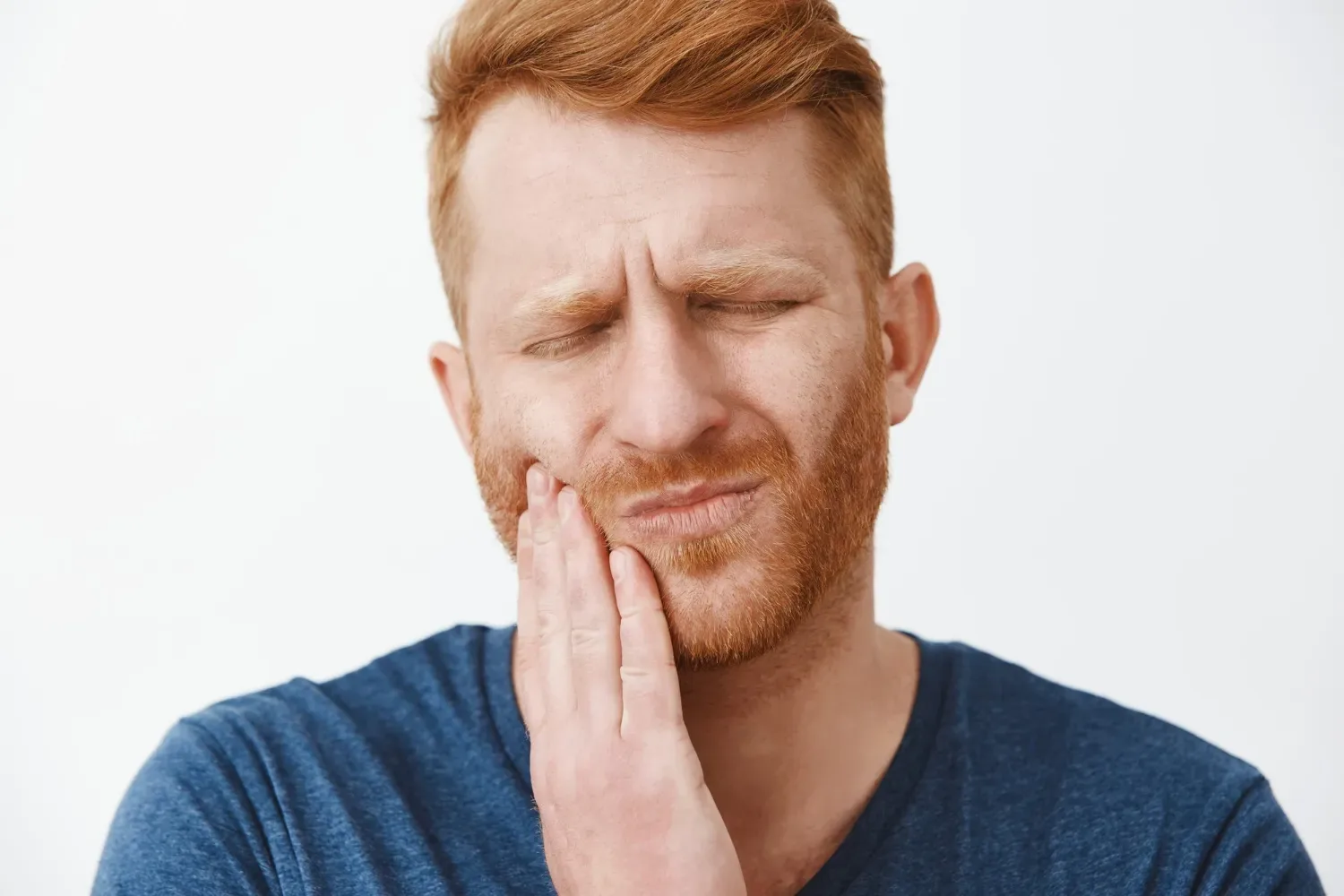 A man wincing with his hand cupped against his jaw
