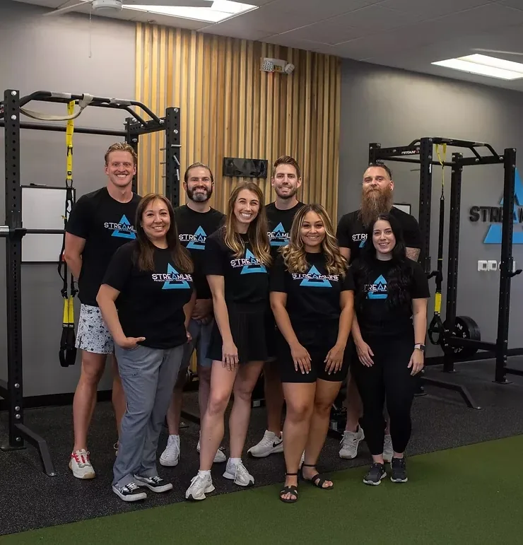 Nine members of the Streamline Performance Physical Therapy staff in matching black tees in front of the power rack on the turf at the Phoenix clinic