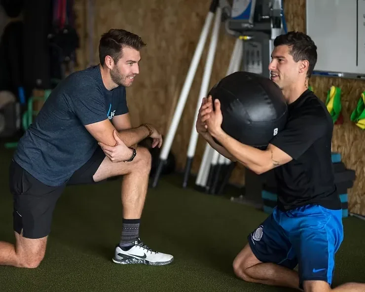 A strength and conditioning coach spotting a client through a split-stance lunge on the turf in Phoenix